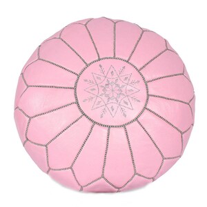 May include: A pink leather pouf with a silver snowflake design. The pouf is round and has a tufted surface.