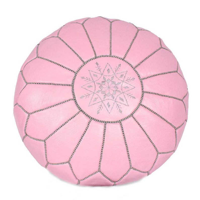 May include: A pink leather pouf with a silver snowflake design. The pouf is round and has a tufted surface.