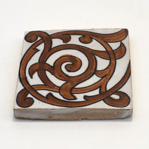 May include: A square ceramic tile with a brown and white design. The tile features a swirling pattern of brown lines on a white background.
