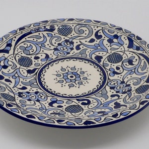 May include: A white ceramic plate with a blue and grey floral pattern. The plate has a raised rim and a centre circle with a smaller floral design.