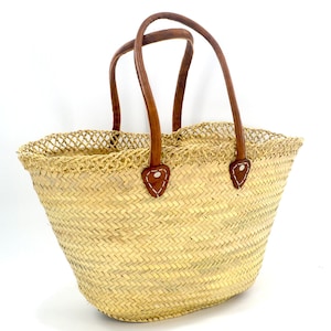 K&ouml;nnte beinhalten: Eine geflochtene Strohtasche mit braunen Ledergriffen. Die Tasche hat ein Fischgr&auml;tenmuster und einen netzartigen Besatz am oberen Rand.