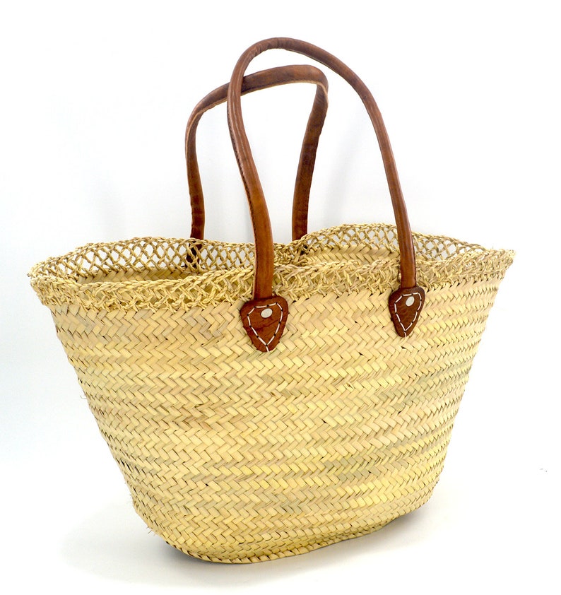 K&ouml;nnte beinhalten: Eine geflochtene Strohtasche mit braunen Ledergriffen. Die Tasche hat ein Fischgr&auml;tenmuster und einen netzartigen Besatz am oberen Rand.
