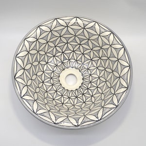May include: Round ceramic sink with a floral pattern in black and gray. The sink has a central drain hole and a light gray rim. The flower design is repeated across the surface.