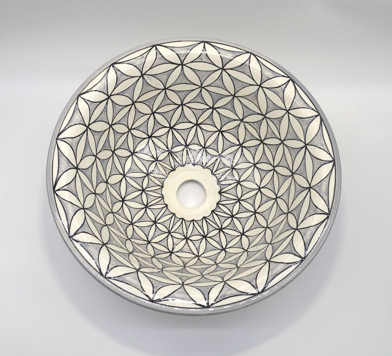 May include: Round ceramic sink with a floral pattern in black and gray. The sink has a central drain hole and a light gray rim. The flower design is repeated across the surface.
