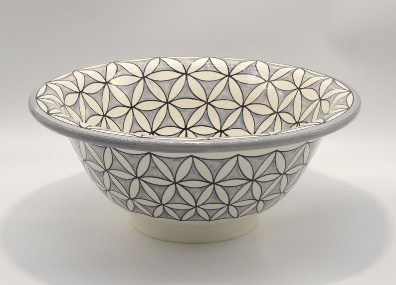 May include: A ceramic bowl with a gray and white floral pattern. The bowl has a wide rim and a footed base. The floral design is repeated around the exterior of the bowl. The rim and base are a solid gray color.