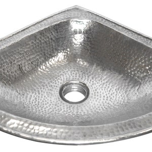 May include: A silver corner sink with a hammered finish. The sink has a rounded rectangular shape and a single drain hole in the centre.