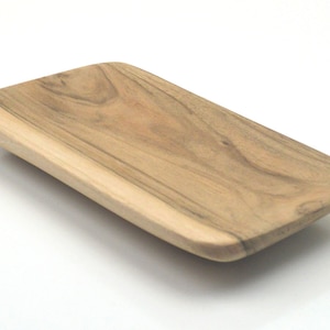 May include: A rectangular wooden serving tray with a natural wood finish. The tray has a slight curve to the edges and is made of a light brown wood.