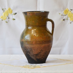 May include: A brown and green glazed ceramic jug with a handle. The jug has a rustic, handmade look.