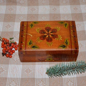 May include: A wooden box with a hand-painted floral design. The box is painted in shades of brown, red, and green. The lid of the box is open, revealing the inside of the box.