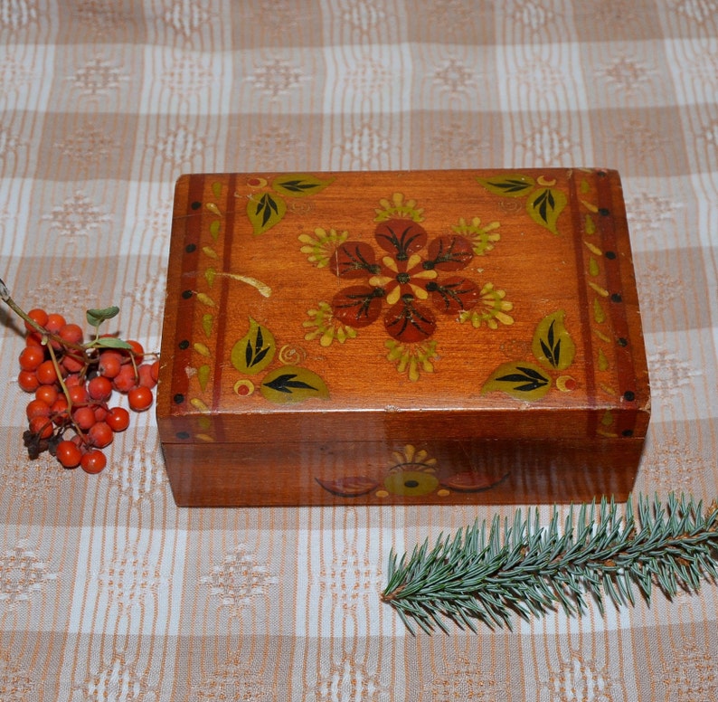 May include: A wooden box with a hand-painted floral design. The box is painted in shades of brown, red, and green. The lid of the box is open, revealing the inside of the box.