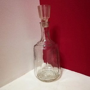May include: A clear glass decanter with a textured surface and a glass stopper. The decanter has a wide base and a narrow neck.