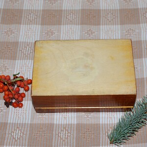 May include: A wooden box with a light brown finish and a dark brown trim. The box is sitting on a checkered tablecloth.