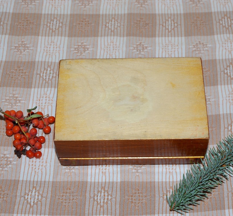 May include: A wooden box with a light brown finish and a dark brown trim. The box is sitting on a checkered tablecloth.