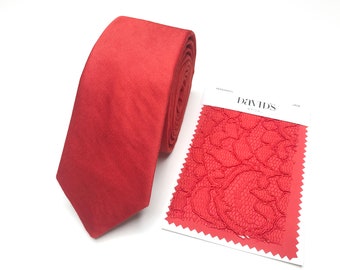 Può includere: Una cravatta di colore rosso corallo con un campione di pizzo rosso corallo abbinato. Il campione di pizzo ha il testo "David's Bridal" stampato su di esso.