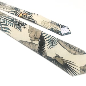 May include: A beige tie with a tropical leaf print in shades of green, brown, and black.