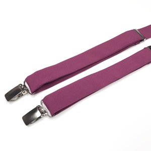 May include: A pair of purple suspenders with silver clips. The suspenders are made of a soft, stretchy fabric.