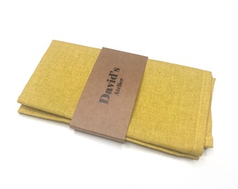 May include: A folded yellow linen napkin with a brown paper band that says "David's Atelier" in black text.