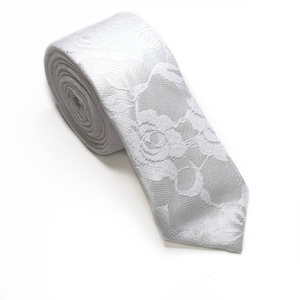 May include: White lace tie with a floral pattern. The tie is rolled up and the tip is pointed.