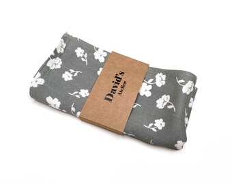 Può includere: Un fazzoletto grigio piegato con un motivo floreale bianco. Un'etichetta di carta marrone con il testo "David's Atelier" è avvolta attorno al fazzoletto. Il fazzoletto è realizzato in un tessuto morbido ed è adatto all'uso quotidiano.