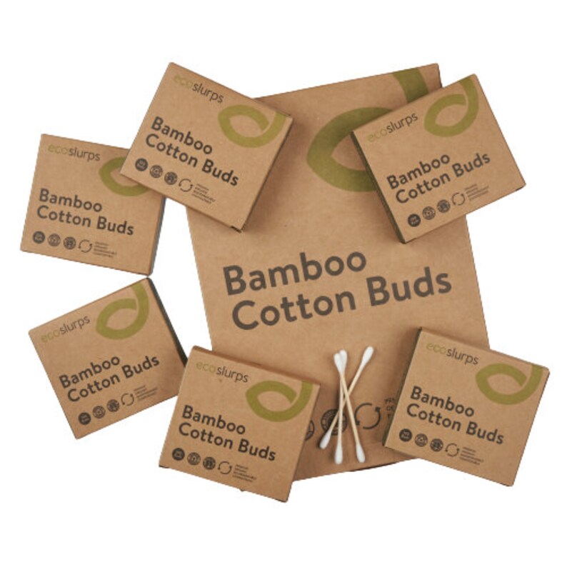 May include: Six brown cardboard boxes with the text "Bamboo Cotton Buds" and the brand name "ecoslurps" printed on them. The boxes are arranged in a scattered pattern on a brown surface. There are also three wooden cotton swabs in the image.