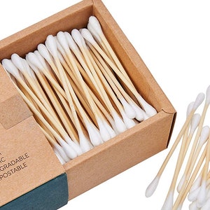 May include: A box of 100 biodegradable and compostable cotton swabs with bamboo sticks. The box is made of brown cardboard and has a green logo with the text "Premium Organic Biodegradable Compostable".