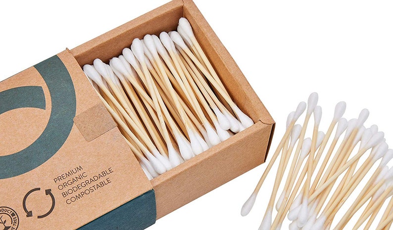 May include: A box of 100 biodegradable and compostable cotton swabs with bamboo sticks. The box is made of brown cardboard and has a green logo with the text "Premium Organic Biodegradable Compostable".