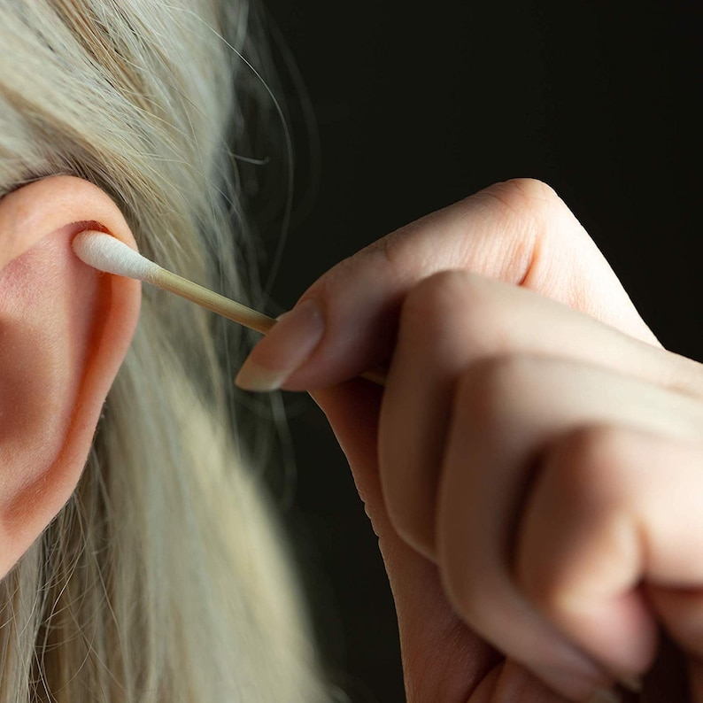 May include: A close-up of a person's hand using a cotton swab to clean their ear.