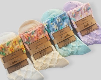 May include: Four pairs of socks with different floral patterns. The socks are all white with a textured design and have a brown tag that says "Saints Combed Cotton Saints".