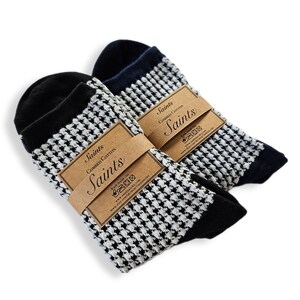 Könnte beinhalten: Zwei Paar Socken mit einem schwarz-weißen Hahnentrittmuster. Die Socken sind aus gekämmter Baumwolle und haben ein braunes Etikett mit dem aufgedruckten Wort "Saints".