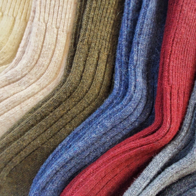 K&ouml;nnte beinhalten: Nahaufnahme von f&uuml;nf Paar Socken in verschiedenen Farben und Texturen. Die Socken sind f&auml;cherf&ouml;rmig angeordnet, wobei die hellste Farbe oben und die dunkelste Farbe unten ist. Die Socken sind aus weichem, gestricktem Stoff und haben eine gerippte Textur.