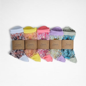 May include: Five pairs of sheer socks in pastel shades: light blue, yellow, pink, purple, and green. Each pair is wrapped with a brown paper band that reads "Saints COMPLETE YOUR STYLE". The socks have a dotted pattern.