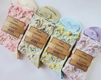 May include: Five pairs of socks with floral patterns. The socks are in different colors: pink, green, light blue, and purple. Each pair has a brown tag with the word "Saints" and "Combed Cotton" printed on it.