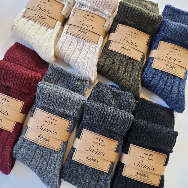 K&ouml;nnte beinhalten: Sortiment von Wollsocken in verschiedenen Farben, darunter Grau, Schwarz, Gr&uuml;n und Burgunderrot. Jedes Paar hat ein braunes Etikett mit dem Text "Saints Lamb's Wool" und einem Logo.