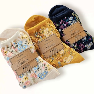 Pode incluir: Três pares de meias de tornozelo com bordado floral. As meias são de cor creme, amarelo e azul marinho. Cada par tem uma etiqueta de papel castanho com o texto "Saints Combed Cotton Saints" impresso nela.