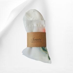 May include: White sheer socks with a floral design and a brown paper band that says "Saints - Complete Your Style".