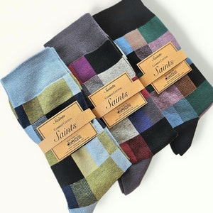 Puede incluir: Tres pares de calcetines con un patrón a cuadros en varios colores, incluyendo azul, verde, rojo y negro. Cada par tiene una etiqueta marrón con el texto "Saints Combed Cotton Saints" e instrucciones de lavado.