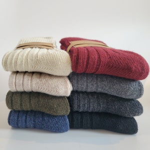 K&ouml;nnte beinhalten: Ein Stapel von acht Paar Socken in verschiedenen Farben, darunter Beige, Rot, Grau, Gr&uuml;n und Blau. Die Socken sind gefaltet und ordentlich gestapelt.