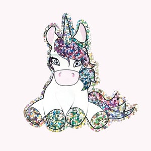 Könnte beinhalten: Ein glitzerndes, regenbogenfarbenes Einhorn mit einer regenbogenfarbenen Mähne und einem Schwanz. Das Einhorn sitzt mit gekreuzten Beinen und hat eine rosa Nase.