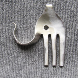 Peut inclure: Une fourchette en argent pliée en forme d'éléphant. Les dents de la fourchette forment la trompe de l'éléphant et le manche est la tête de l'éléphant. L'œil de l'éléphant est un trou dans le manche.