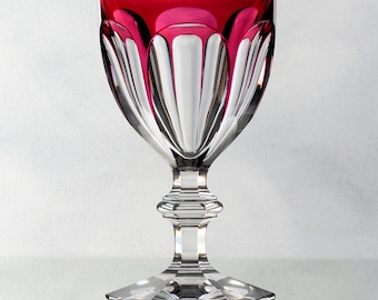Op de afbeelding: Een helder glazen wijnglas met een dieprode rand en een facetgeslepen ontwerp. Het glas heeft een hoge, slanke steel en een zeshoekige voet.