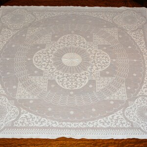 May include: White lace tablecloth featuring an elaborate floral design. The tablecloth is square in shape and has a delicate, embroidered pattern.