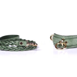 May include: A sage green leather dog leash with a braided design and a gold-colored clasp. Next to it is a matching dog collar with gold-colored metal rings and hardware. The collar and leash are on a white background.