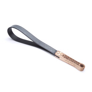 May include: A black leather paddle with a wooden handle. The handle has a geometric pattern carved into it.