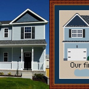 May include: A cross-stitch pattern of a two-storey house with a garage, porch, and landscaping. The text "Our first home" is below the house. The pattern is framed in a brown wood frame.