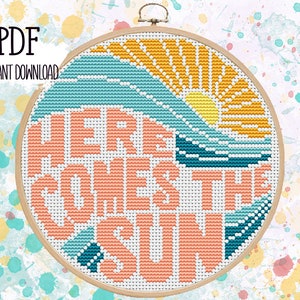以下が含まれることがあります： カラフルな夕焼けと「Here Comes The Sun」というテキストが桃色のオレンジで書かれたクロスステッチパターンです。
