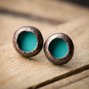 May include: A pair of handcrafted copper stud earrings. Each earring features a hammered, textured copper exterior with a vibrant turquoise interior. The earrings are round and have a rustic, artisan aesthetic, perfect for everyday wear.