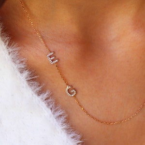 May include: A gold chain necklace with two initial charms. The charms are set with small, clear stones and spell out the letters "E" and "G".