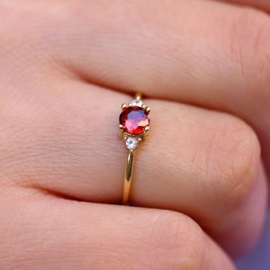 May include: A gold ring with a red gemstone and two smaller white gemstones.