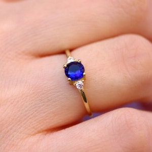 May include: A gold ring with a blue gemstone and two smaller white gemstones.