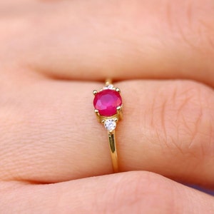 May include: A gold ring featuring a red ruby gemstone and two smaller white gemstones.